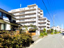 青空に映える「コスモ西亀有」の外観。落ち着いた住宅街に佇む7階建マンションです。周囲には植栽や緑があり、穏やかな住環境が魅力。上千葉砂原公園にも隣接し、自然を身近に感じながら暮らせる住まいです。